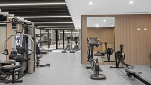 Une salle de sport moderne équipée de divers appareils d’exercice, dotée d’un murmiroir et offrant une vue sur l’extérieur.