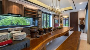 A modern kitchen with a long wooden countertop, built-in appliances, and a large window offering a view of greenery. - Intragama Villa (Cisarua)