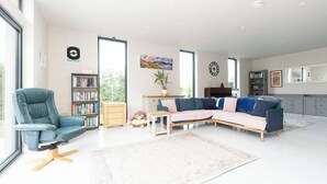 Un saló modern amb un sofà modular, un butac armchair còmode, una biblioteca i una finestra gran.