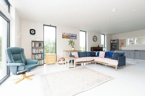 A modern living room with a sectional sofa, a plush armchair, a bookshelf, and a large window. - Fairway Lodge for up to 8 adults and 2 children (St. Andrews)