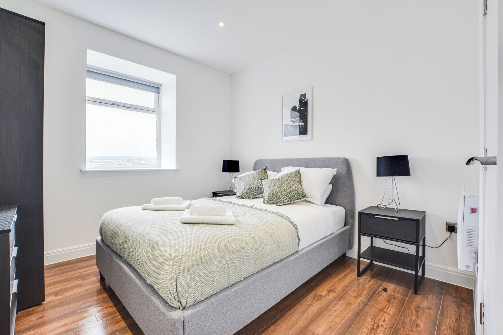 Une chambre à coucher moderne avec un grand lit, une table de chevet, une lampe et une vue sur l’extérieur.