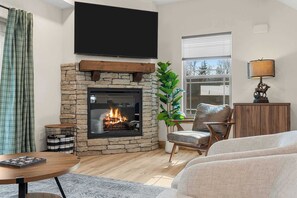 Una sala de estar con chimenea de piedra, un televisor de pantalla plana, un sillón cómodo y un ventanal grande.