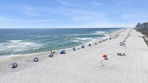 En strand med rader av parasoller och strandstolar, en sandstrand och havet i bakgrunden.