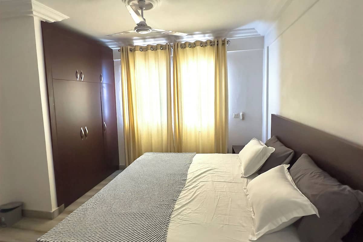 Une chambre à coucher avec un lit, un ventilateur de plafond, des rideaux et une armoire.