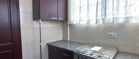 Una cocina con armarios oscuros, una estufa a gas y un ventanal con cortinas.