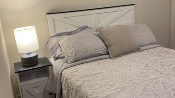 A neatly made bed with a patterned bedspread, a bedside lamp, and a nightstand with a drawer.