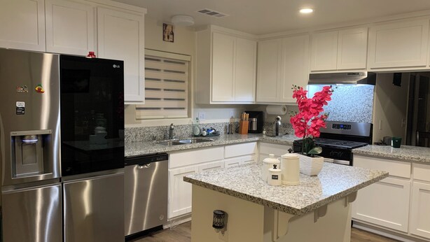 A modern kitchen with white cabinetry, stainless steel appliances, a granite countertop, and a small island with a sink. - Spacious 5BR/3BA Family Home in Riverbank (Riverbank)