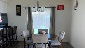 A dining area with a round table, six chairs, and a chandelier. There is a kitchen in the background, a window with curtains, and a rug on the floor. - Spacious 5BR/3BA Family Home in Riverbank (Riverbank)