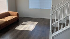 A spacious living room with a wooden floor, a sofa, a staircase, and a large window with blinds. - Spacious 5BR/3BA Family Home in Riverbank (Riverbank)