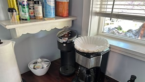 Eine Küche mit Kaffeemaschine, einer Schale mit Kaffeekapseln und verschiedenen Küchenutensilien in einem Regal.