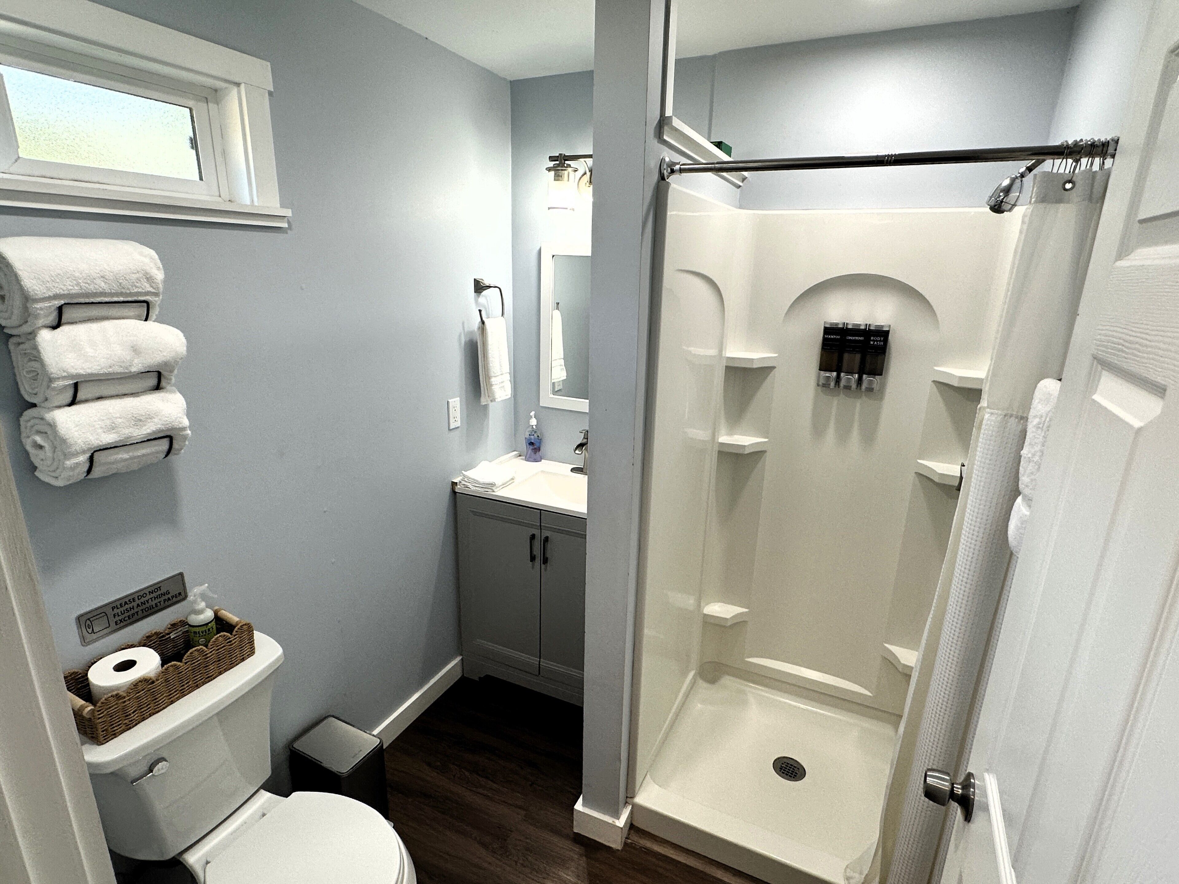 A bathroom with a toilet, sink, mirror, and shower.