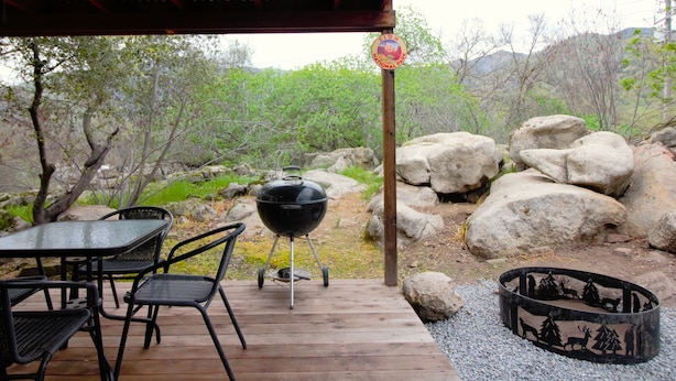 Eine Holzterrasse mit Grill, Tisch und Stühlen im Freien sowie einer Feuerstelle.