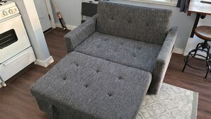 Ein graues, gepolstertes Sofa mit einer Noppenstruktur, ein Holzboden und ein gemustertes Teppich.