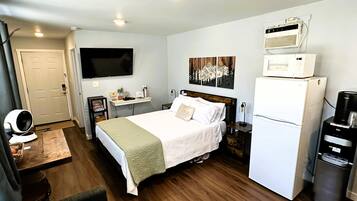 A hotel room with a bed, a TV, a microwave, a refrigerator, and a coffee machine.