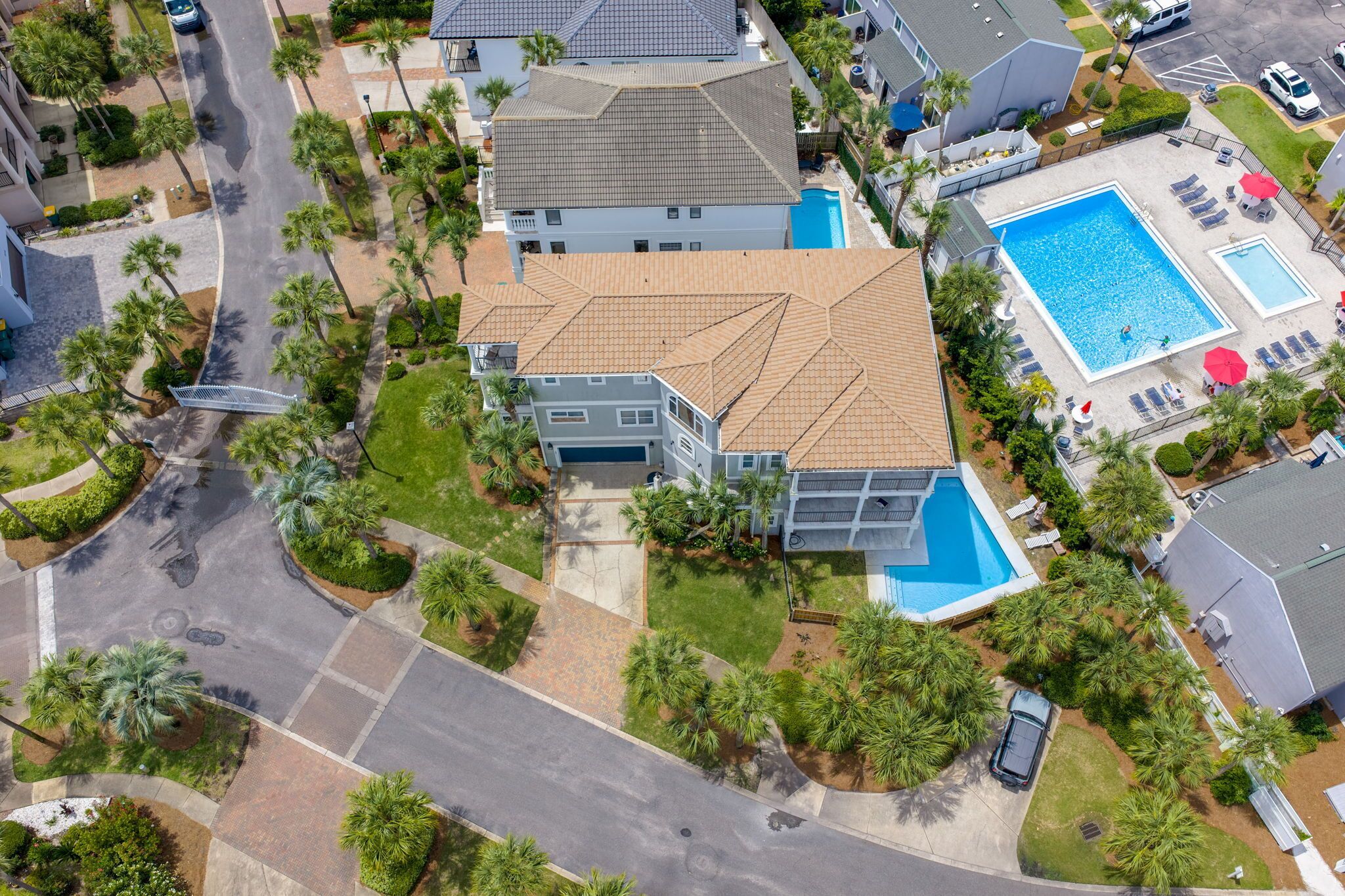 An aerial view of a residential area with a large house featuring a swimming pool, a garage, and a well-maintained lawn.