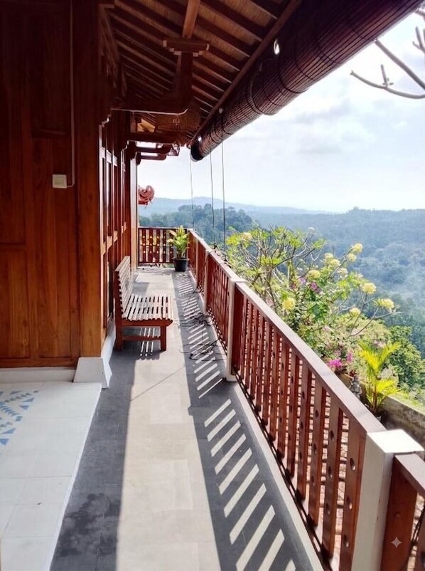 Un balcone in legno con una panchina, una ringhiera e vista su un paesaggio montuoso.
