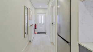 Un pasillo con paredes blancas, una puerta al final y un extintor a la izquierda.