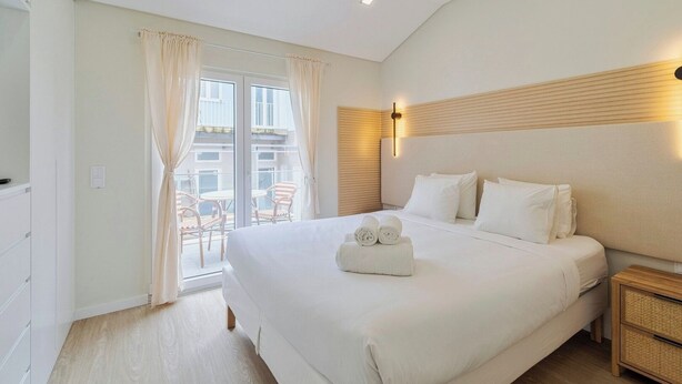 Una habitación de hotel con una cama grande, un cabecero de madera, una mesita de noche y un balcón con sillas.