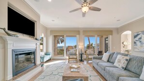 A living room with a fireplace, sofa, and a ceiling fan. - Large Beachfront 3B Condo | Heated Pool & Hot Tub (Holmes Beach)