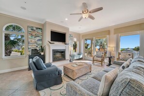 A spacious living room with a fireplace, comfortable seating, a flat-screen TV, and large windows.