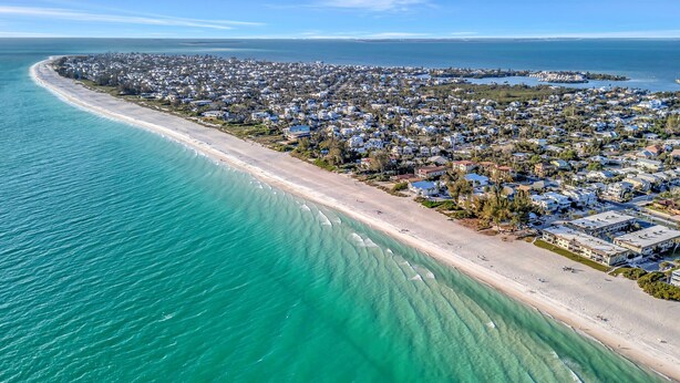 An aerial view of a coastal residential area with a beachfront, houses, and clear blue waters. - Large Beachfront 3B Condo | Heated Pool & Hot Tub (Holmes Beach)