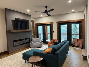 A modern living room with a sectional sofa, a flat-screen TV, a fireplace, and large windows. - Modern home with Mountain Views, Hot Tub, EV outlet, Family and Dog friendly, (Mineral Bluff)