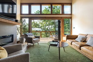 A spacious living room with a large window, a fireplace, and a cozy seating area. - Modern home with Mountain Views, Hot Tub, EV outlet, Family and Dog friendly, (Mineral Bluff)
