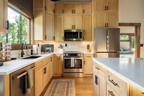 A modern kitchen with wooden cabinets, stainless steel appliances, and a large window providing natural light. - Modern home with Mountain Views, Hot Tub, EV outlet, Family and Dog friendly, (Mineral Bluff)