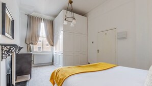 Quarto com cama, guarda-roupa, radiador e janela com cortinas.
