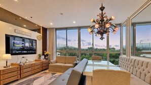 A modern living room with a sofa, a glass-top dining table, and a TV mounted on the wall. - Summit By SanLiving - 2BR (Jakarta)