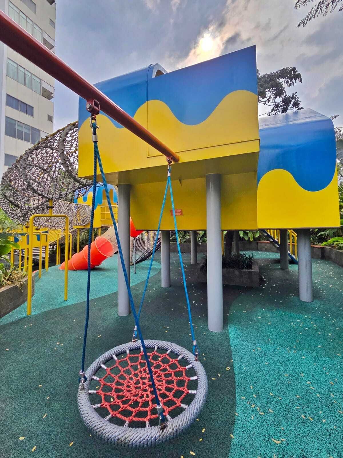 A playground with a netted climbing structure, a swing, and a slide.