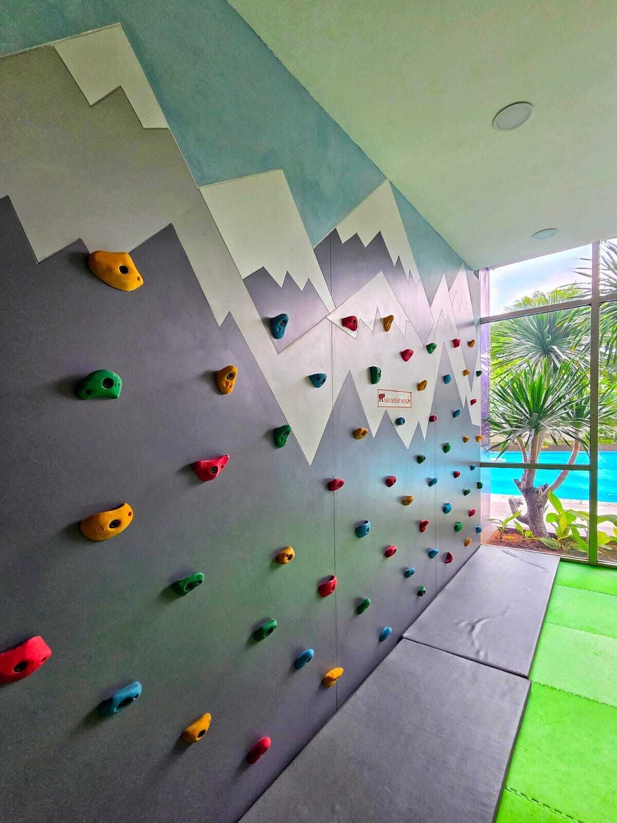 Un mur d’escalade doté de prises de différentes couleurs, un motif géométrique et une vue sur une piscine à l’extérieur.