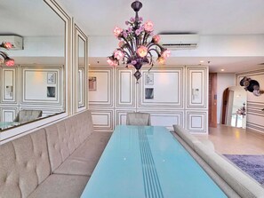 Uma área de refeições com uma mesa comprida, assentos acolchoados, um candelabro e painéis decorativos nas paredes.