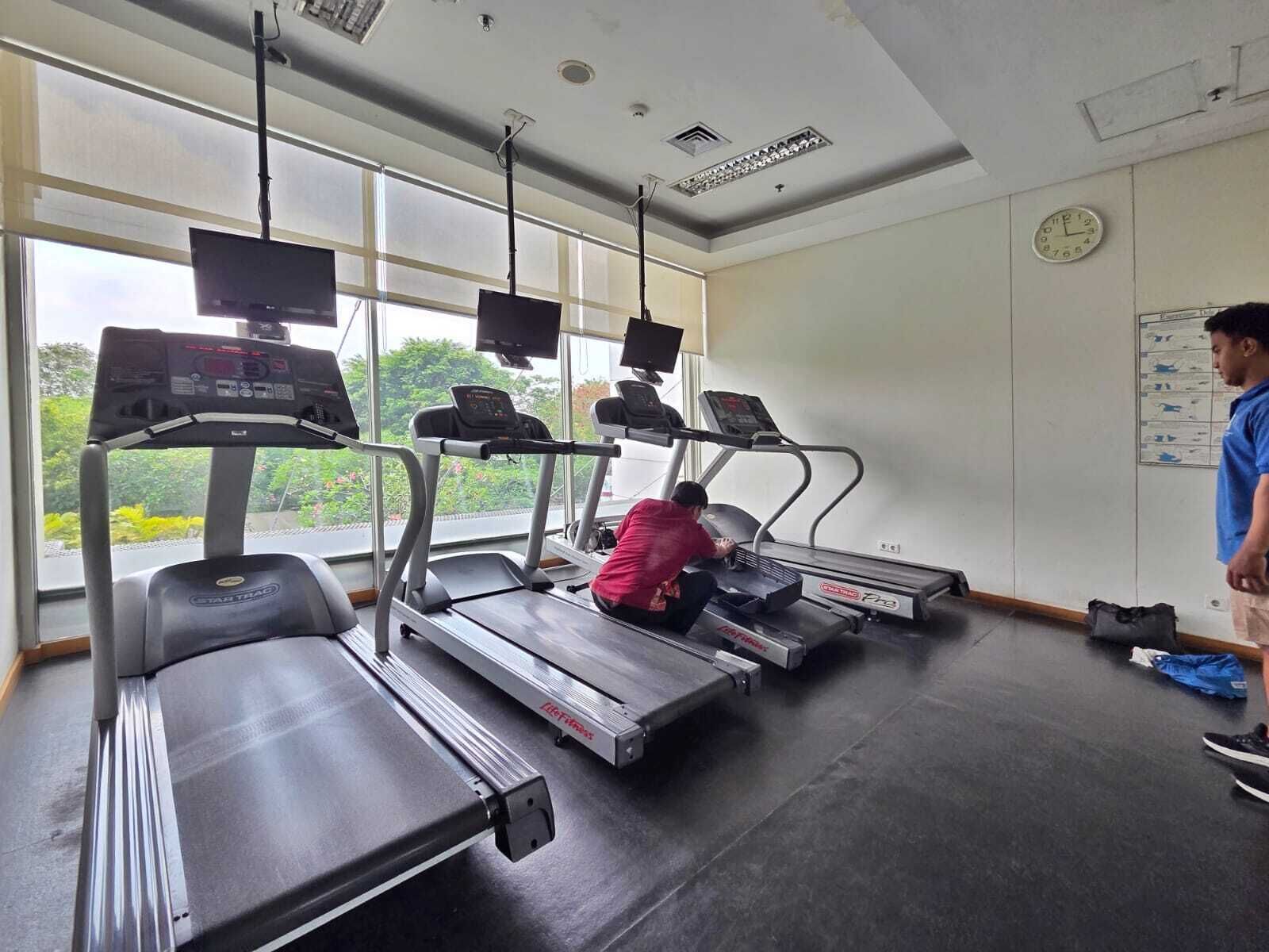 A gym with treadmills, a wall clock, and a window with a view of greenery.
