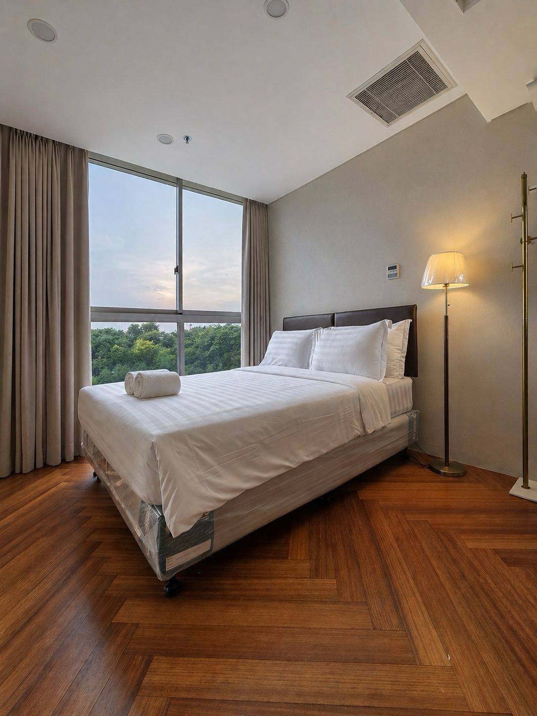 A hotel room with a large bed, a standing lamp, and a view of the outdoors.