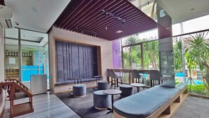 A modern lounge area with seating, a large window, and a view of greenery. - Summit By SanLiving - 2BR (Jakarta)