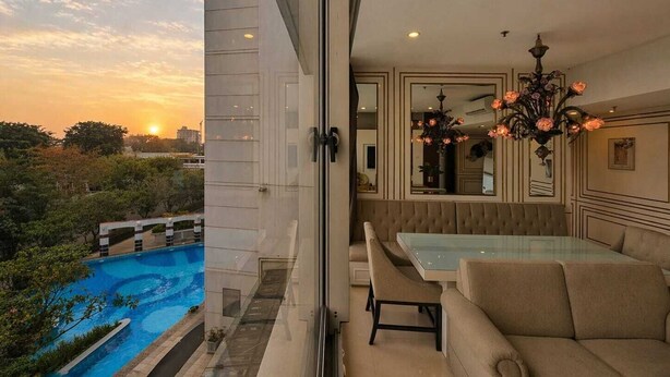 A modern interior with a glass table, beige sofas, and a chandelier. - Summit By SanLiving - 2BR (Jakarta)
