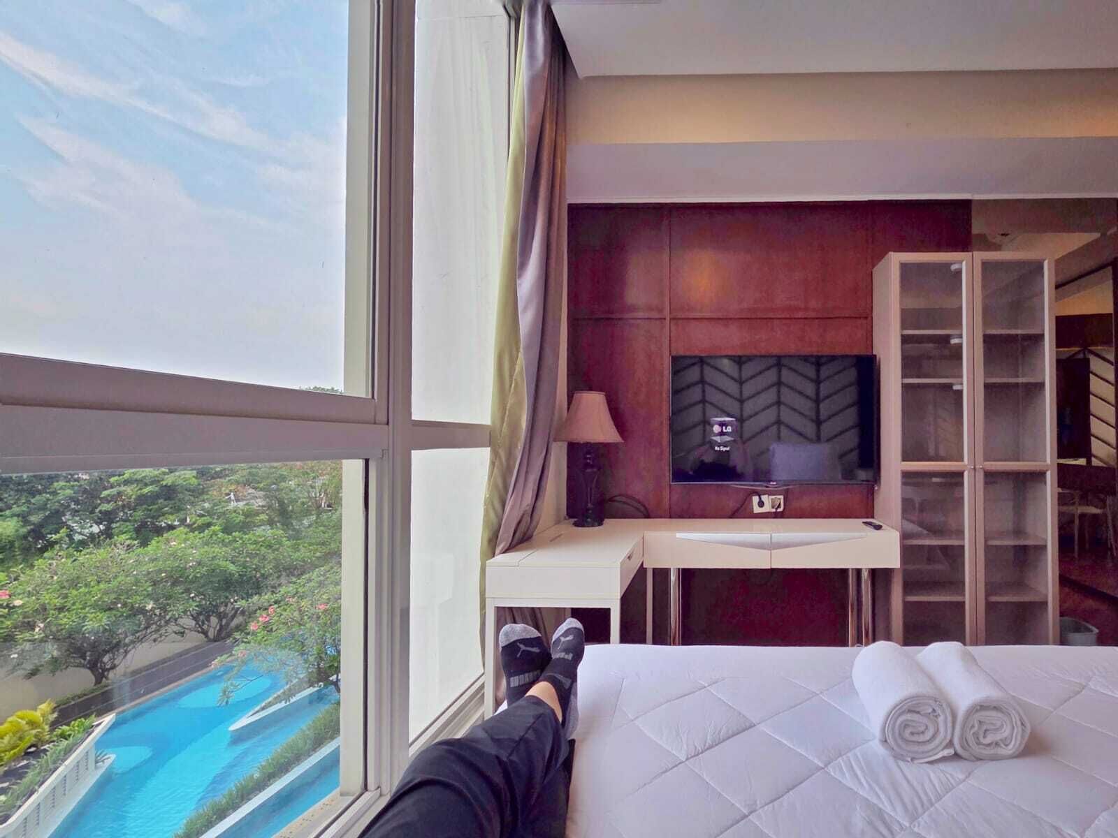 A hotel room with a bed, a TV, a desk, and a view of a swimming pool.