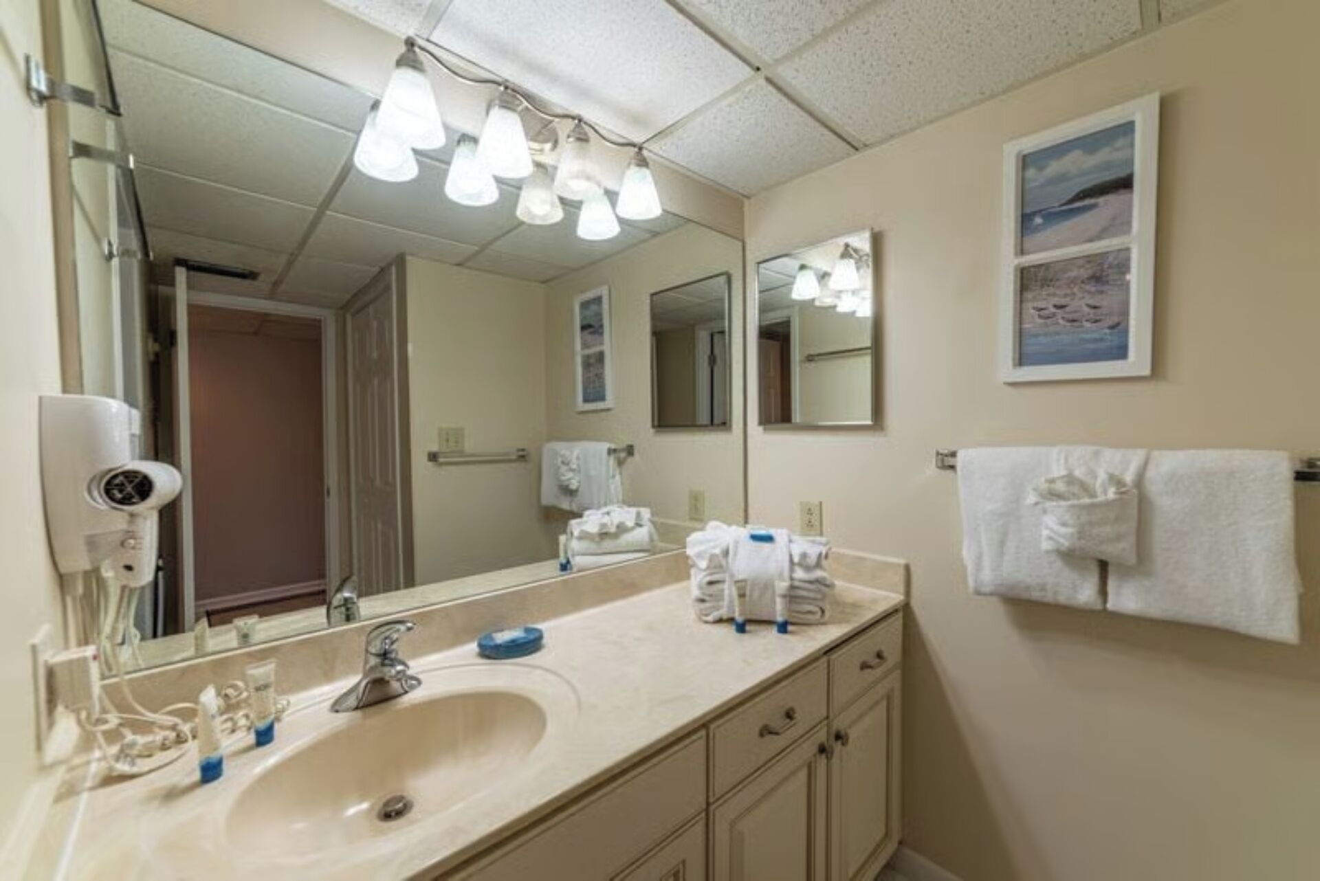 Un baño de hotel con un espejo grande, un lavamanos y un perchero para toallas.
