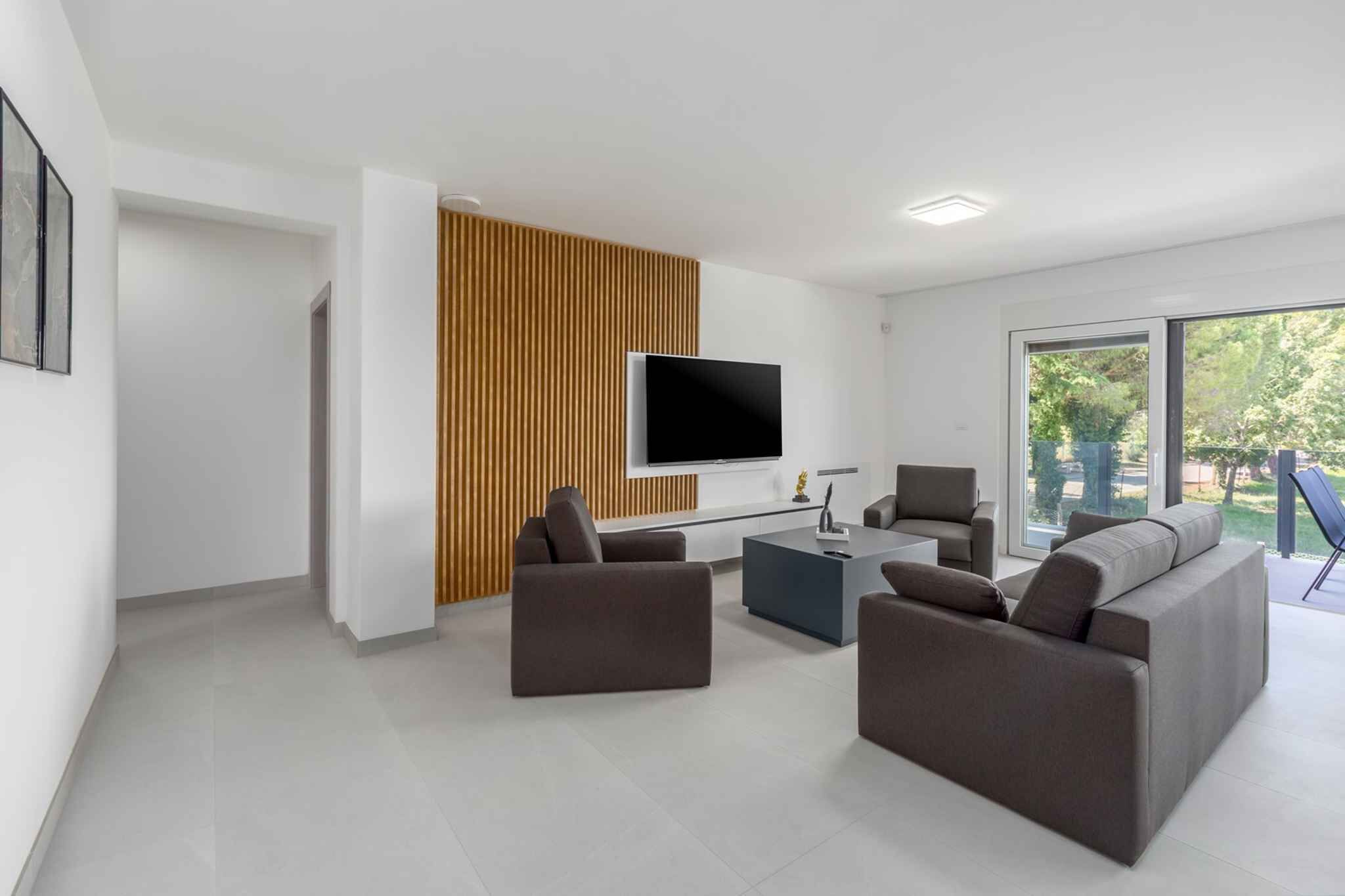 A modern living room with a flat-screen TV mounted on a wooden panel wall, a gray sofa, a coffee table, and a chair.
