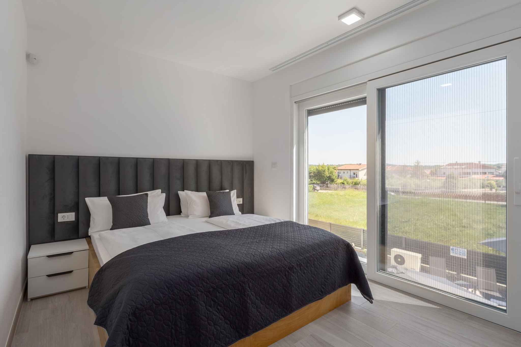 A modern bedroom with a large bed, a nightstand, and a sliding glass door to a balcony.