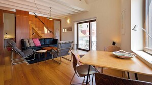 Un espace de vie moderne avec un plancher en bois, un canapé noir, une table à manger en bois et un escalier.