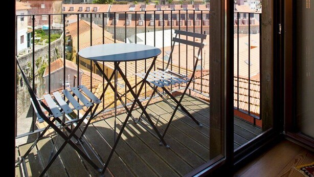 Un balcon avec une table et des chaises, donnant sur un paysage urbain avec des bâtiments et de la verdure.