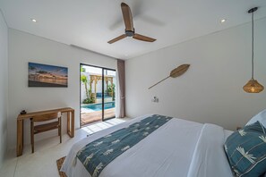 A bedroom with a bed, a desk, a ceiling fan, a large window with a view of a swimming pool, and a wall-mounted decorative leaf. - Villa Dara (Canggu)
