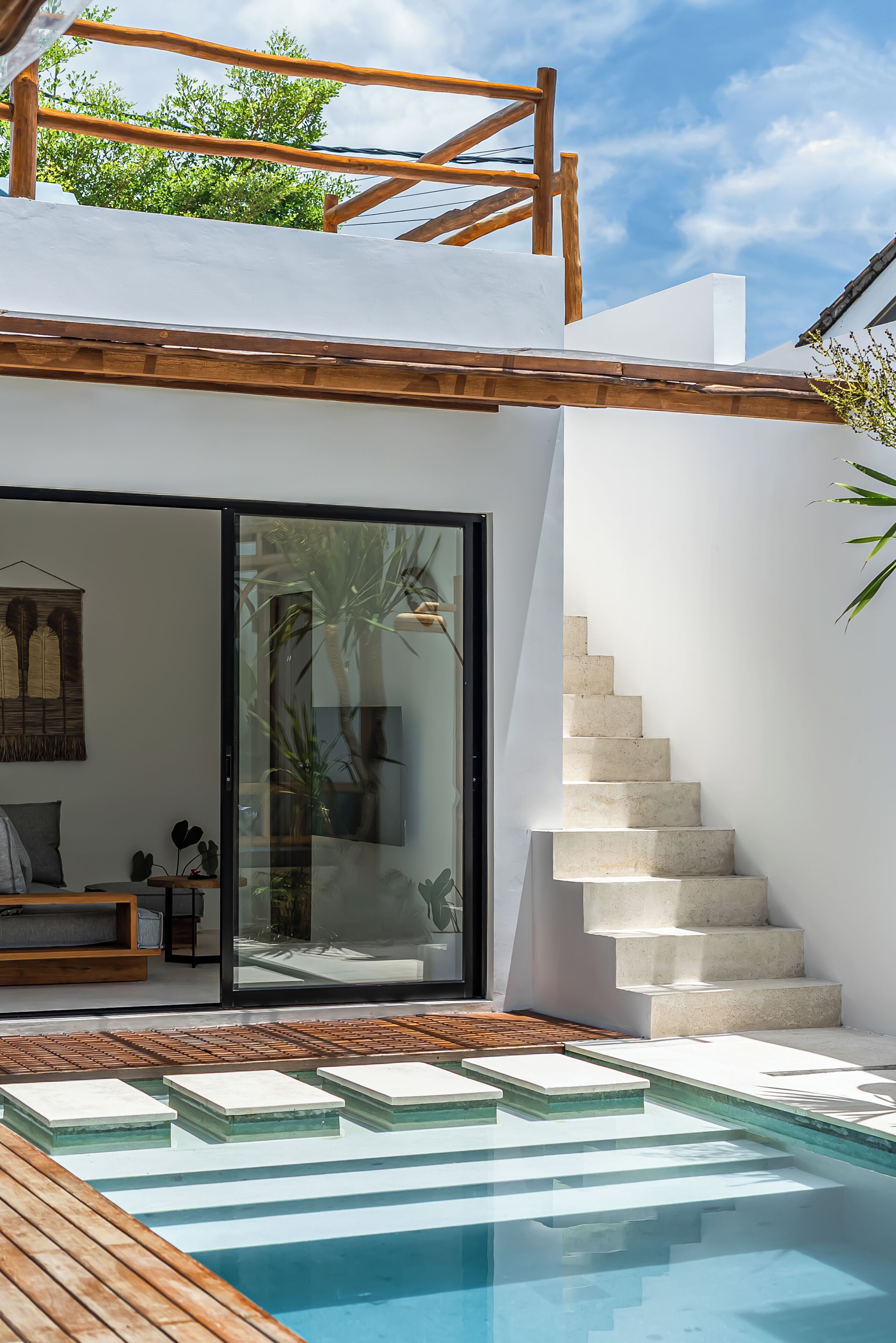 A modern outdoor pool area with a wooden deck, a glass door entrance, and a staircase leading to a second level.