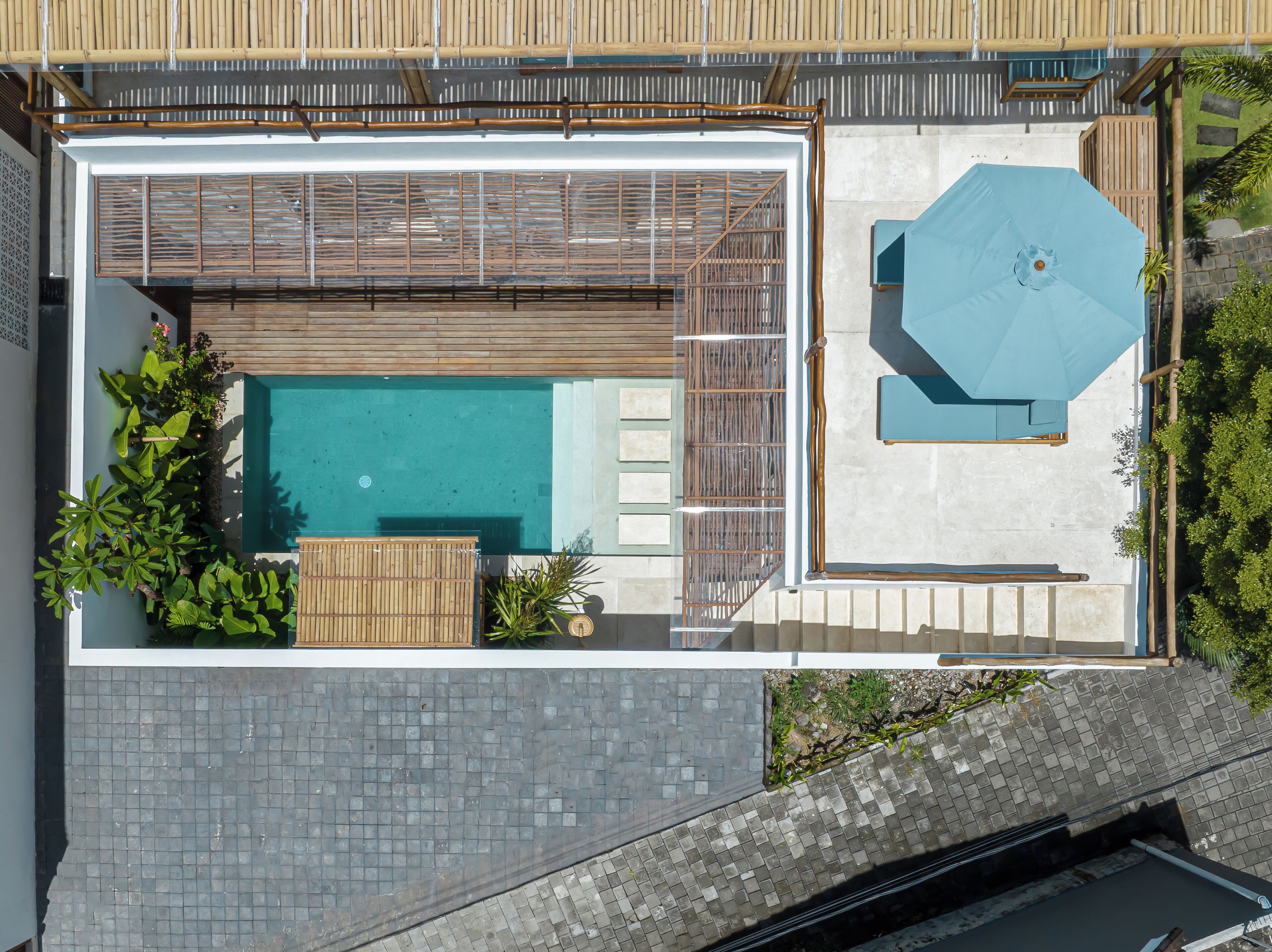 Vue aérienne d’un espace piscine sur le toit, avec une terrasse en bois, un coin salon et un parasol bleu.