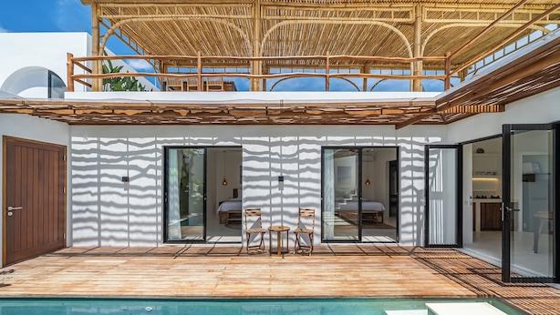 Una casa moderna con piscina, terraza de madera y un espacio exterior cubierto con sillas.