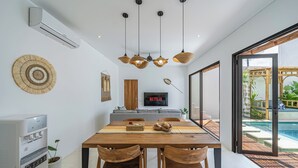 Un comedor moderno con una mesa de madera, dos sillas de madera, un dispensador de agua y un televisor fijado a la pared.