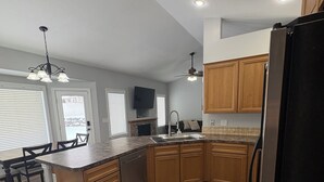 Une cuisine moderne avec des meubles en bois, un réfrigérateur noir et une cheminée en pierre.