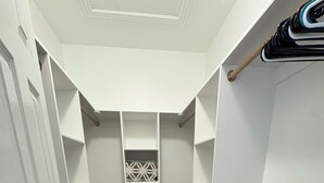 Un dressing accessible sans porte, avec des étagères blanches, une échelle en bois et un sol recouvert de moquette.